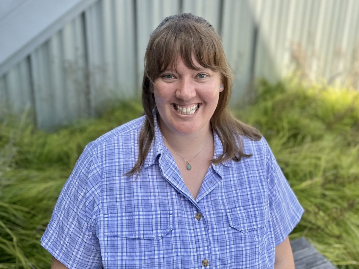 Photo of Hannah Smith-Wright smiling standing outdoors near green grass and a metal fence.